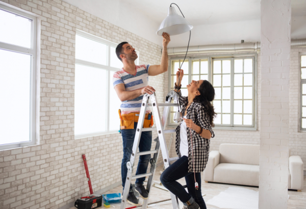 a man and a woman on a ladder, hanging a light up