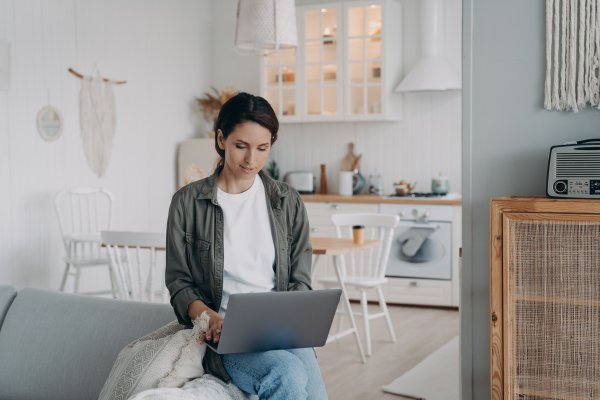 woman sitting on edge of couch working on a laptop