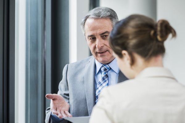 man in a suit talking to a woman in a suite and gesturing to the documents in her hand