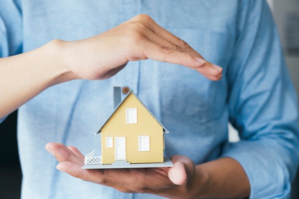 a yellow miniature house being held between two hands. One hand is hovering over the top and the other is resting under the house
