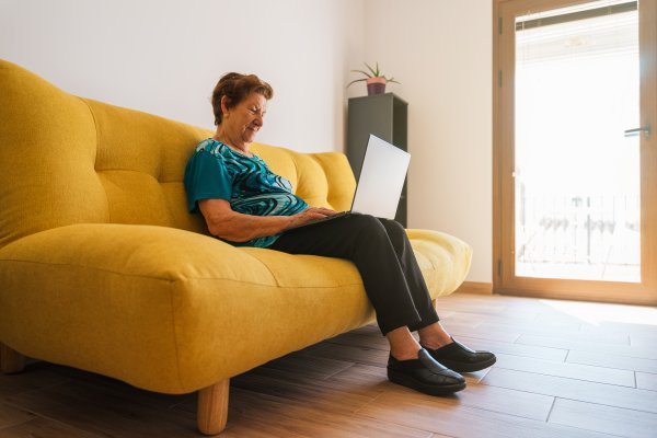 senior woman sitting on a yellow couch with a laptop in her lap