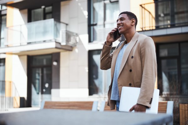 young man talking on his cell phone, holding a laptop in the city